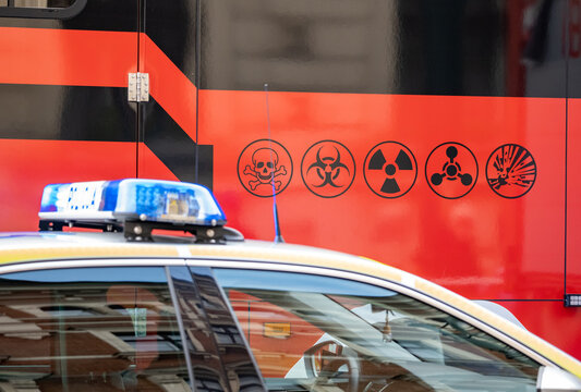 Police car beside a hazardous materials emergency response vehicle with biohazard, radiation and toxic warning symbols close-up of public safety CBRN incident containment and crisis response no people