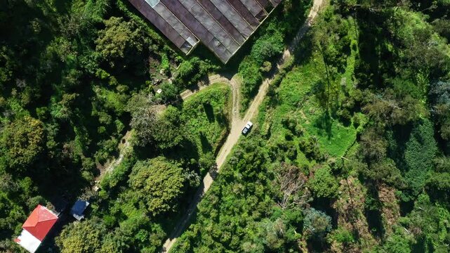 Aerial view of a greenhouse alongside a dirtroad, moving up to show the whole scene