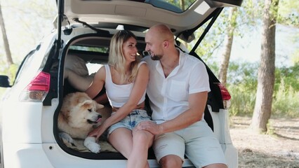 Happy lovely couple with Akita Inu sitting in the open trunk car © Vlad