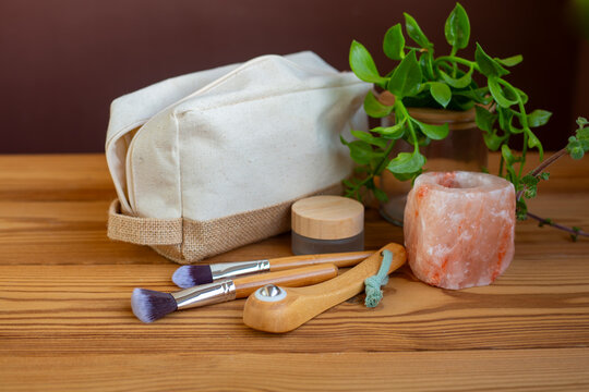 A natural linen beauty case on a wooden background with salt crystal candle holder a wooden roller for regenerating facial massage and bamboo makeup brushes. A zero-waste beauty concept
