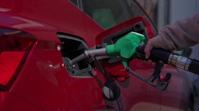 Woman's hand refueling a modern red car at gas station oil crisis, inflation