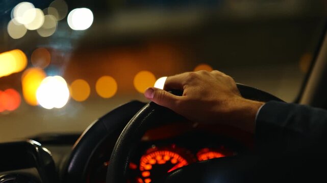 Male hand on car steering wheel. Man listening the music on the radio. Dashboard panel. City lights. Right hand drive car. Traveling, trip, night life concept. Real time