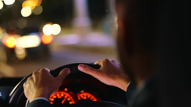 Man driving car in the evening and looking on the road while holding hands on the steering wheel. Right hand drive car. Traveling, trip, night life concept. Real time