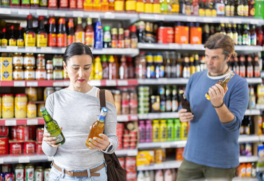 Couple of adult man and woman choosing bottles of beer in grocery store