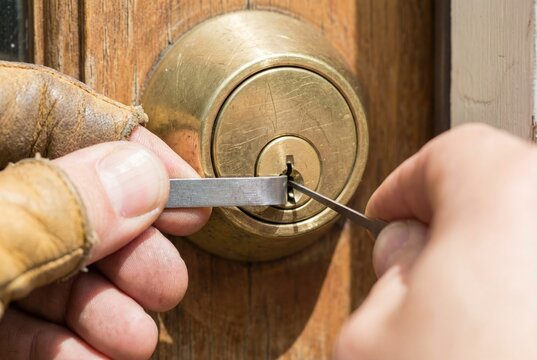 Close up of gloved hands using tools to pick a brass door lock cylinder
