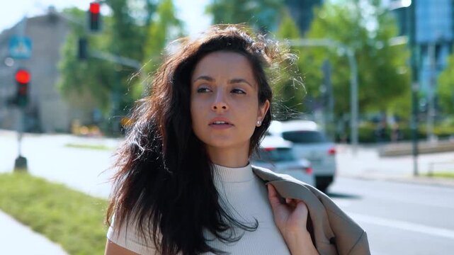 Young businesswoman taking off jacket while going down street. Attractive lady put blazer on one shoulder. Lifestyle concept. Real time