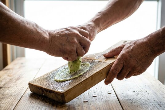Chef grating fresh green wasabi root on a traditional wooden shark skin grater