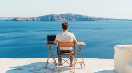 Obraz premium Man focused on a laptop, working from an outdoor balcony overlooking the vast blue ocean and distant island in Santorini, Greece