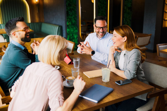 Four friends or colleagues are laughing and talking together at a table in a modern cafe