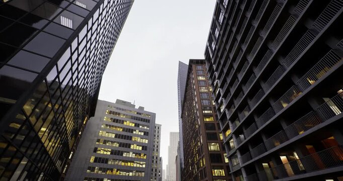 Narrow urban canyon with lit windows, twilight city scene showing stacked balconies and reflective glass, urban planner scenario glimpsed through offices, busy