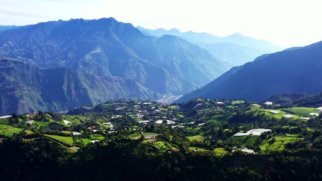 Aerial view of valley full of greenhouses and meadows with a bright green color in spring surrounded by high mountains of the Andes ridge in Ecuador, South America