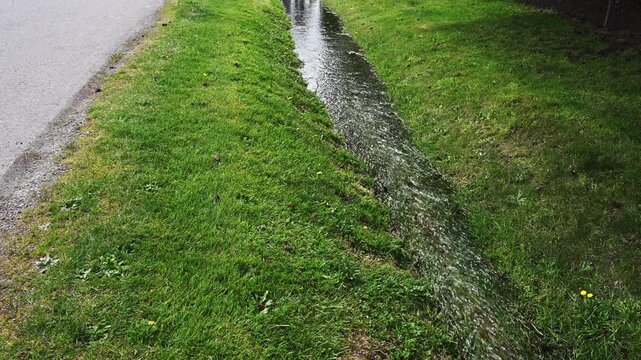 Water running in grass ditch next to street, part of municipal stormwater system
