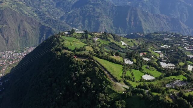 A small dirtroad is running along a cliff, separating a valley full of greenhouses and agricultural fields with the village Banos de agua Santa below