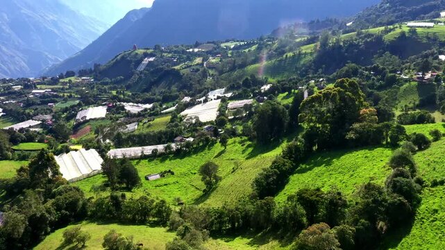 Aerial view of a valley with tree patches, greenhouses and meadows: bright green background in springtime on a sunny day