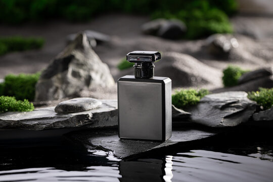 Unisex golden perfume reflecting in the water surrounded by stones.