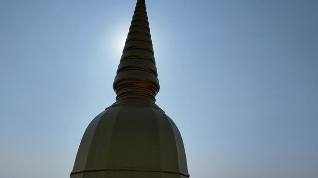 Cinematic low angle drone movement revealing the grand Maha Chedi Sri Sarakham temple against a glowing sunset backlight.