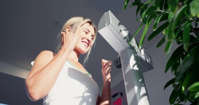 Female athlete standing on electronic scales weighing herself in modern gym