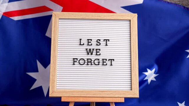Somber Australian flag backdrop with text LEST WE FORGET on letter board. Respectful message for memorial ANZAC campaigns. Concept of remembrance and honor