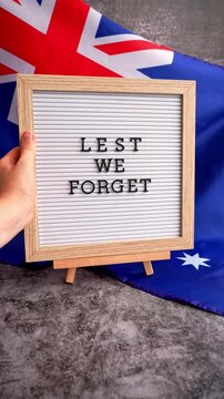 Somber Australian flag backdrop with text LEST WE FORGET on letter board. Respectful message for memorial ANZAC campaigns. Concept of remembrance and honor