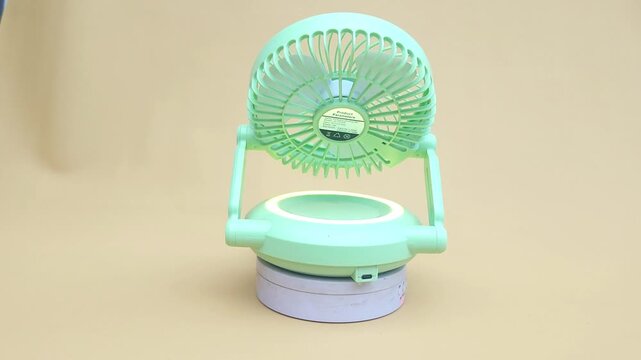 Featuring a pastel blue mini portable fan that rotates slowly on a white rotating stand, providing a clear and detailed 360-degree view. Its compact, modern, and ergonomic design looks elegant against