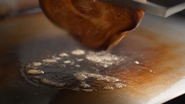 A spatula smashes a juicy smash burger patty on a grill with seasonings.