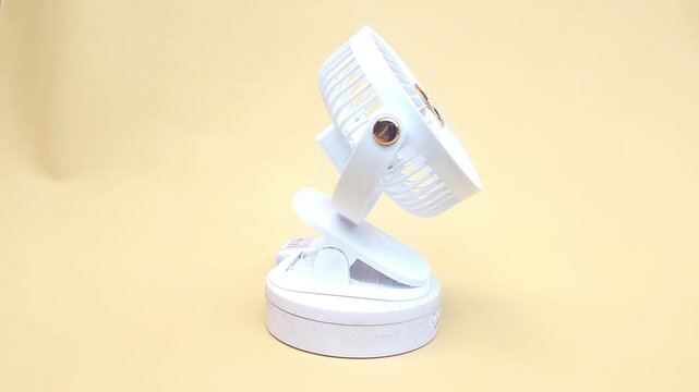 Close-up of a compact, portable mini fan displayed on a turntable against a soft yellow background. Ideal for personal cooling at home, in the office, or while traveling. Perfect for use in advertisin