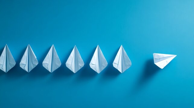 Paper planes aligned in a row with one paper glider flying in different direction on blue background symbolizing leadership innovation and breaking away from conformity in business