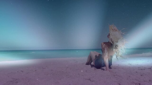 Female model reclining on sand, breeze lifting hat, light bands sweeping across body for travel