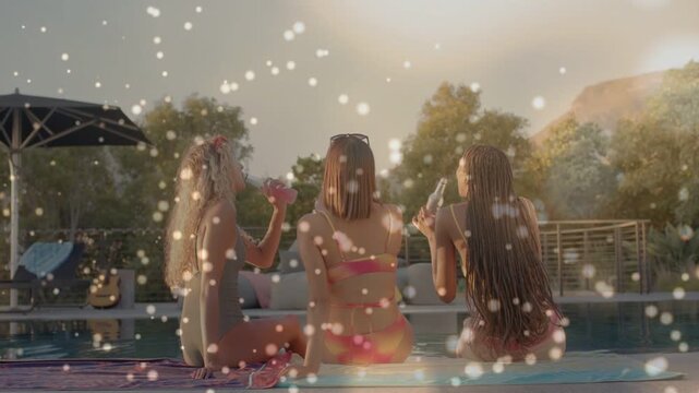 Three women sitting poolside, chat starting and raising drinks while sparkle drifting, lifestyle
