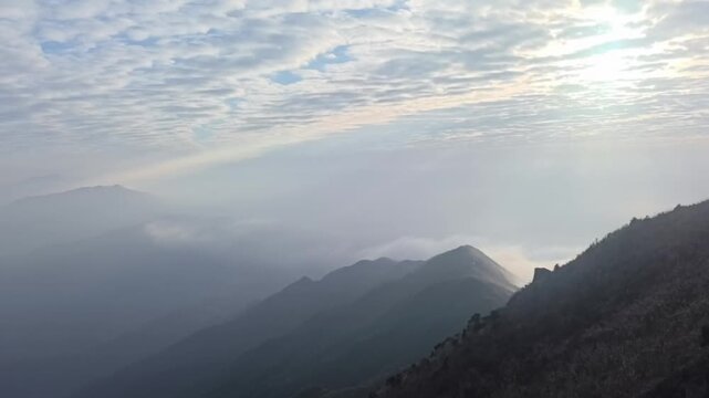 A breathtaking timelapse capturing double layer clouds flowing rapidly over mountain ridges under a clear sky in China.