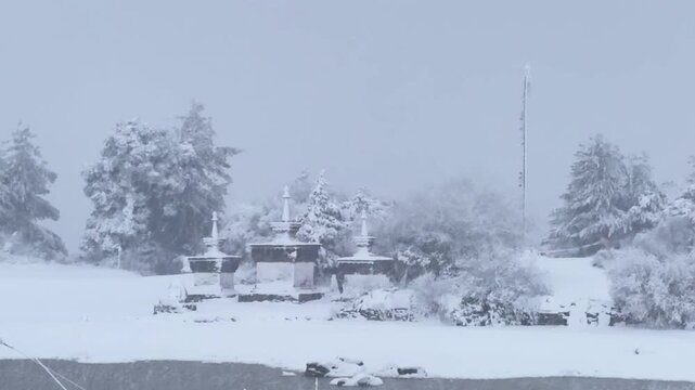 Peaceful cinematic footage of heavy snow falling over traditional Tibetan Buddhist stupas in a winter landscape.