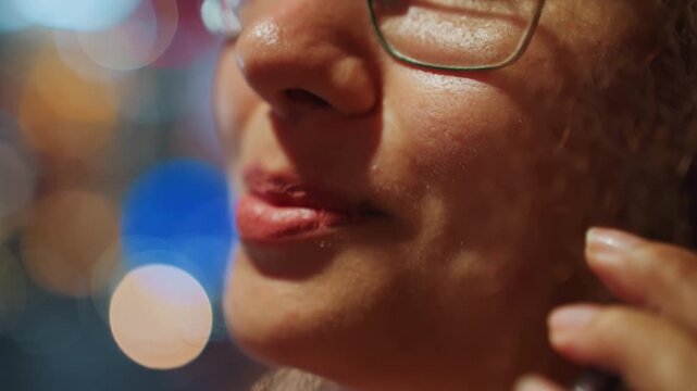 Closeup lips speaking into phone with neon bokeh backdrop, intimate urban night message, subtle smile and mouth movements, glasses rim visible, soft warm skin texture, candid voice moment