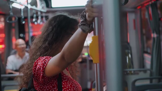 Woman on crowded night bus holding pole, thoughtful gaze in red polka dress and glasses, ambient neon reflections, interior metal rail and yellow stop button, blurred passengers in background,