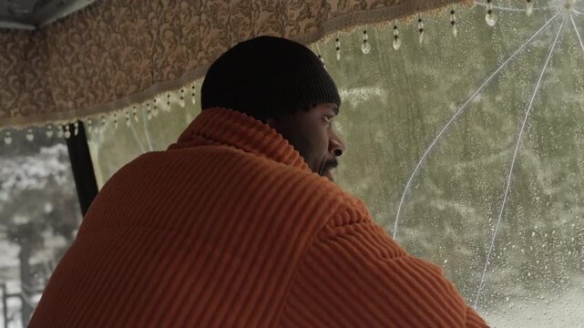 Solitary driver contemplates stormy winter landscape. Observer pauses to absorb cold rain and snow outside vehicle. Contemplative man gazes through icy glass during solitary winter rainstorm