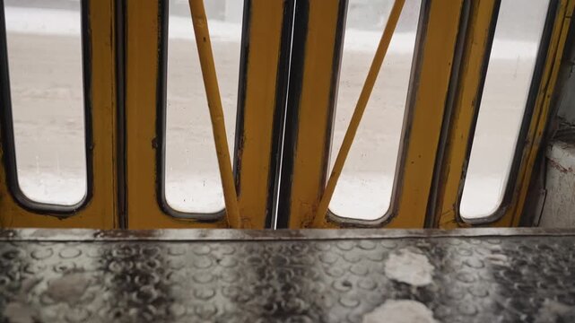 Closeup yellow bus door wet step revealing textured studs and salt residue, worn metal tread and scuff marks under soft light slow pan captures traction pattern and sheen, maintenance crew