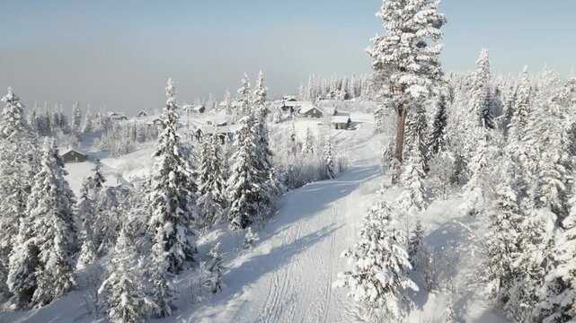 Aerial 4K fly-past a snowy mountain road on a misty Scandinavian cabin village in morning sunlight, Danebu, Valdres, Norway