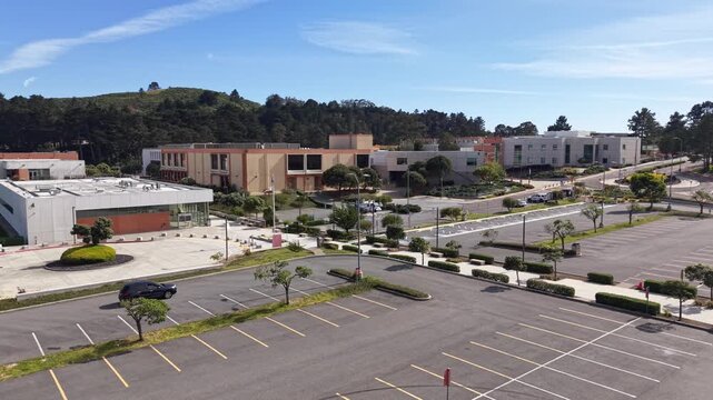 Aerial perspective of the modern architectural buildings and the nearly empty parking lot of Skyline College in San Bruno, California, on a sunny day.