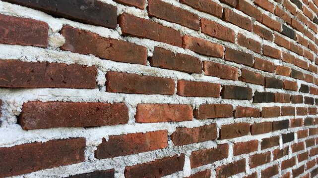 Weathered brick wall shows aged, rustic charm. Mortar lines reveal time's gentle wear. Red bricks stand strong, textured and worn. Ideal for vintage, industrial, or architectural themes. background, 