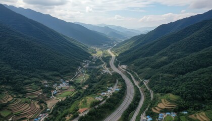 Fototapeta premium Curving highway winding through lush mountainous valley with small settlements.