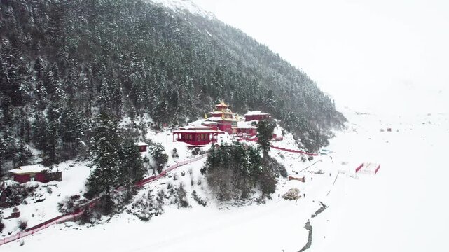 Drone view of Galong temple (Galongsi) in snowing day, red temple wall with golden rooftop in white snow mountain in Bomi County, Nyingchi, Tibet, China. 4k real time footage, travel concept.