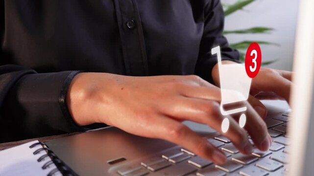 Detail of female hands typing on a laptop with a shopping cart animation and notification of the number of items added.