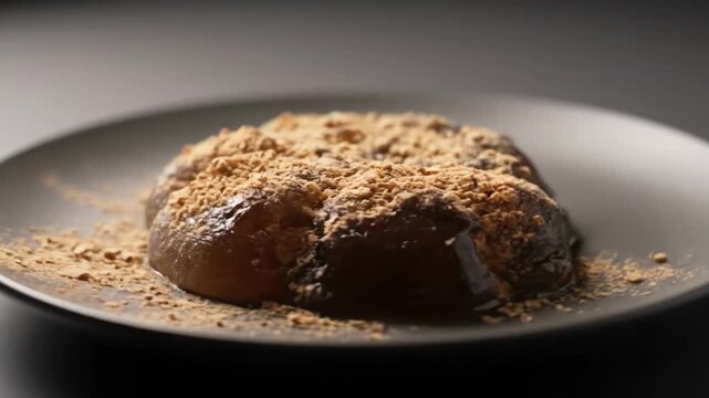 Close-up of traditional japanese warabimochi (bracken starch dumpling) dessert covered in kinako powder, served on a dark gray plate in a dramatic studio setting.