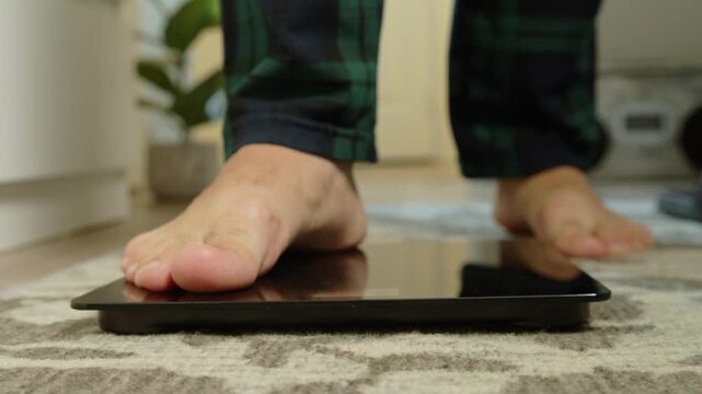 Detailed macro shot: male bare feet step onto a modern bathroom scale in the morning. Concept of healthy lifestyle, weight management and daily self-monitoring 4K