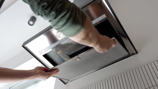 Hands remove a metal filter from a range kitchen hood in a home kitchen. Concept of appliance cleaning maintenance and household care.