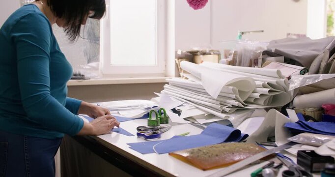 Cutting textile. Atelier work. Female dressmaker creating fabric pattern on studio desk. Seamstress preparing garment pieces for sewing.
