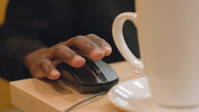 Hand on mouse beside mug, closeup of fingertip navigating laptop interface, cable connected mouse touching wooden desk, warm indoor lighting, programmer checking messages during coffee break