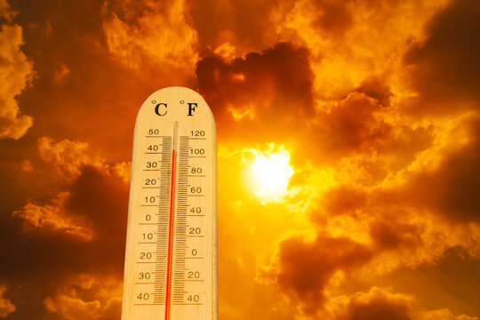 A thermometer measuring high temperature against a background of an orange summer sky.