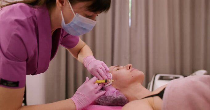 Beauty care. Rejuvenation procedure. Specialist in protective gloves mask making botulinum toxin injection on woman face skin using cotton pads.