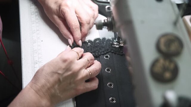 Professional sewing. Garment making. Tailor hands decorating black corset with lace. Precision needle work on electric stitching machine.