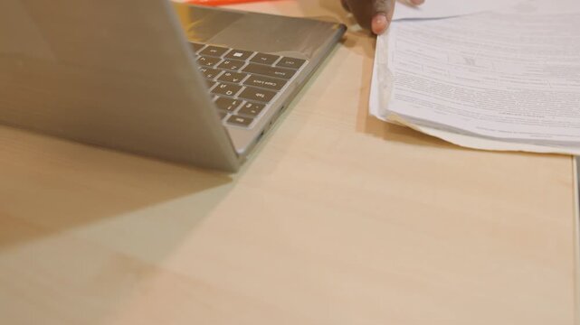 Laptop and test paper on desk, closeup of silver laptop keyboard beside printed exam sheet, pen and circled answers visible, warm indoor lighting, minimal wooden surface, quiet study atmosphere